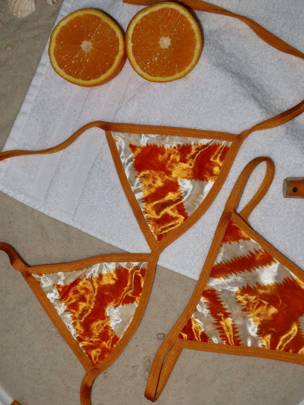 Handmade orange and white velvet bikini set on towel, with fresh orange halves on sand