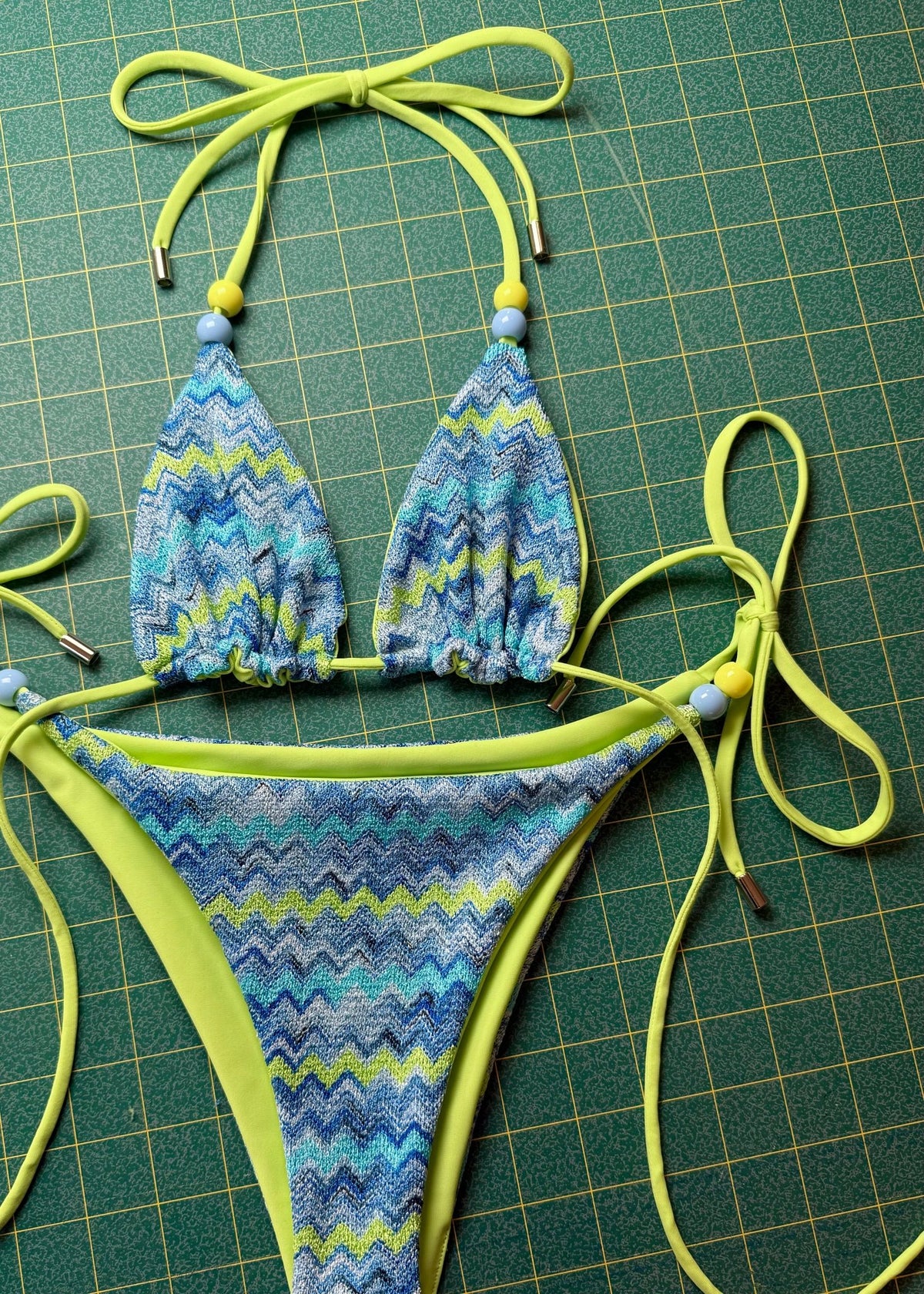 Handmade reversible bikini set with blue and green zigzag pattern and beaded ties on green grid background