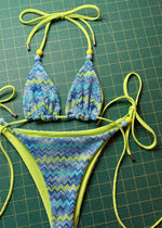 Handmade reversible bikini set with blue and green zigzag pattern and beaded ties on green grid background