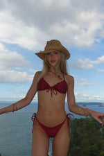 Woman in handmade red bikini and straw hat posing outdoors with ocean and tropical landscape view