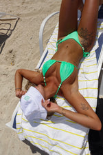 Woman lounging on beach chair in green handmade bikini with bead accents, sunbathing on sand.