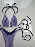 Lavender string bikini set with tie straps and metallic tips on a flat surface