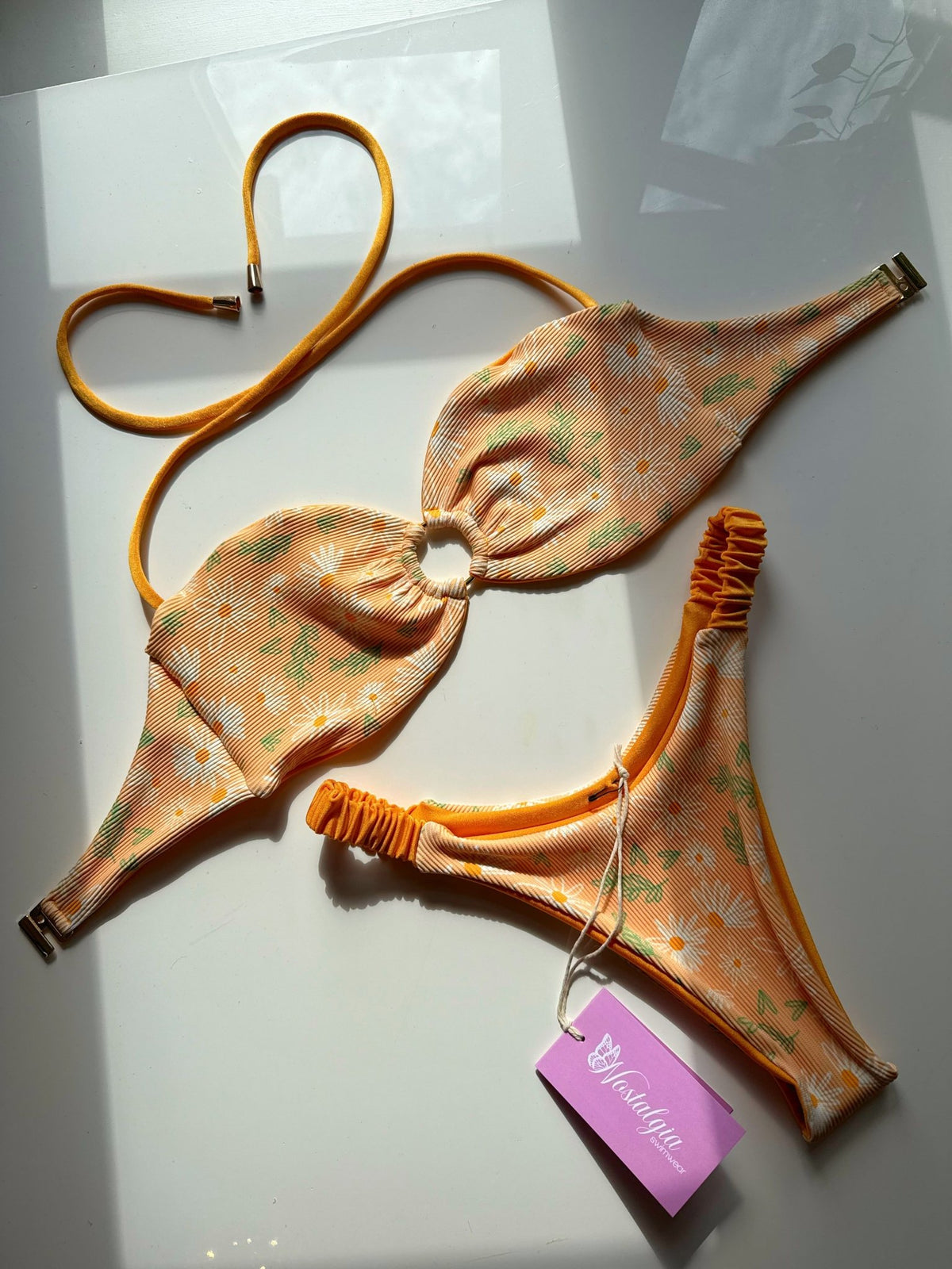 Handmade reversible floral bikini set with daisy print and yellow trim, displayed on white surface.