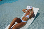 Woman lounging in a handmade reversible bikini on poolside chair in shallow water