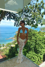 Woman in a light blue bikini top and sheer lace skirt with ocean and tropical view