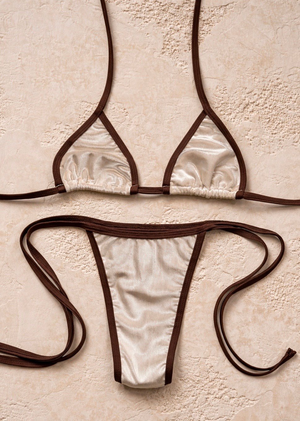 Handmade reversible bikini set with cream fabric and brown trim on neutral textured background