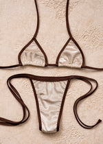 Handmade reversible bikini set with cream fabric and brown trim on neutral textured background