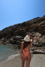 Woman in orange bikini and sun hat on a rocky beach, handmade reversible swimwear
