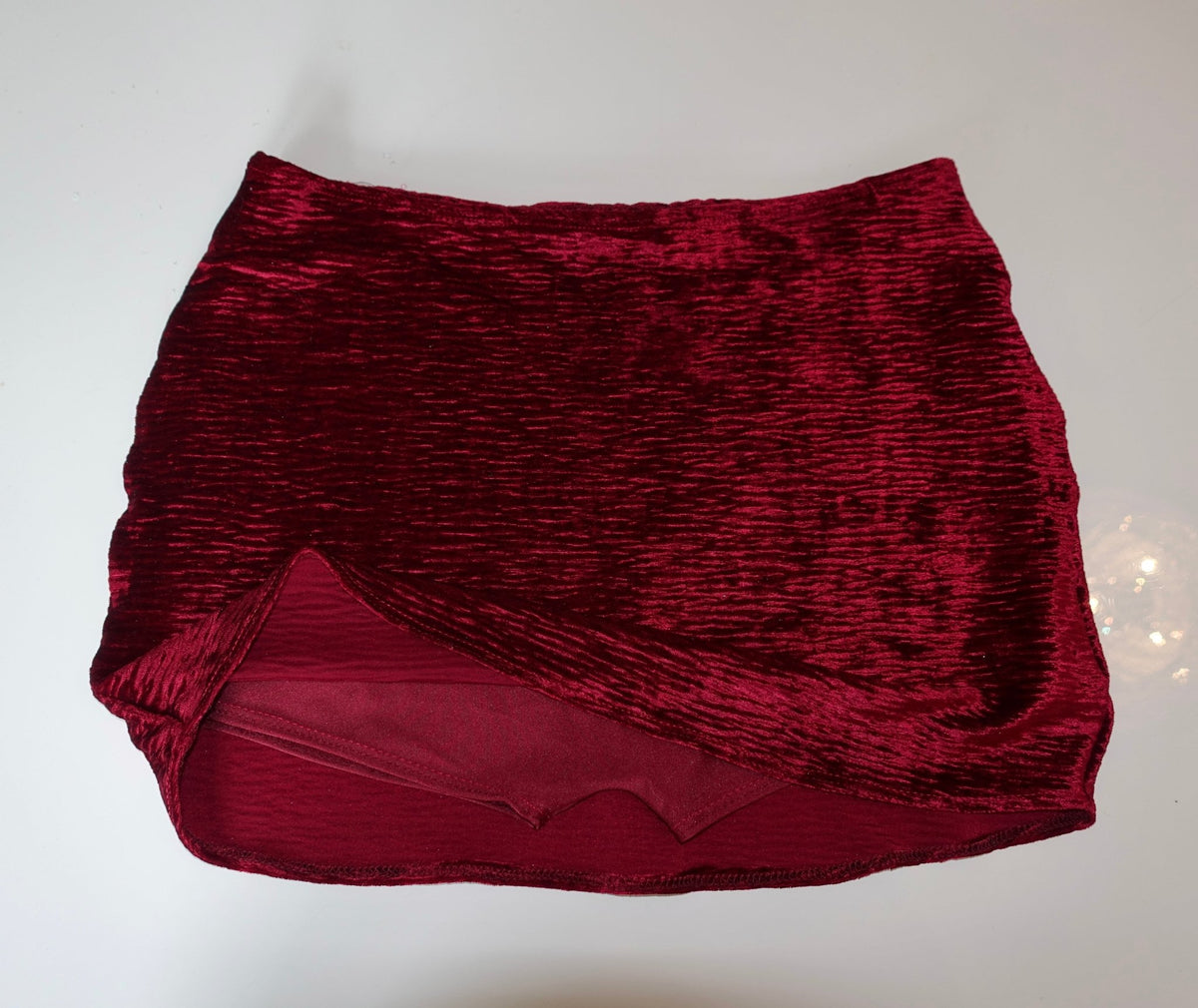 Red velvet mini skirt with textured fabric and wrap-style front, laid flat on white background