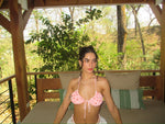 Woman in pink handmade bikini top sitting outdoors on patio daybed with green forest background