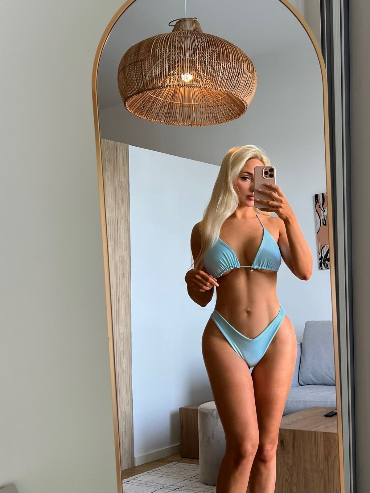 Woman in light blue handmade bikini posing for mirror selfie in modern living room
