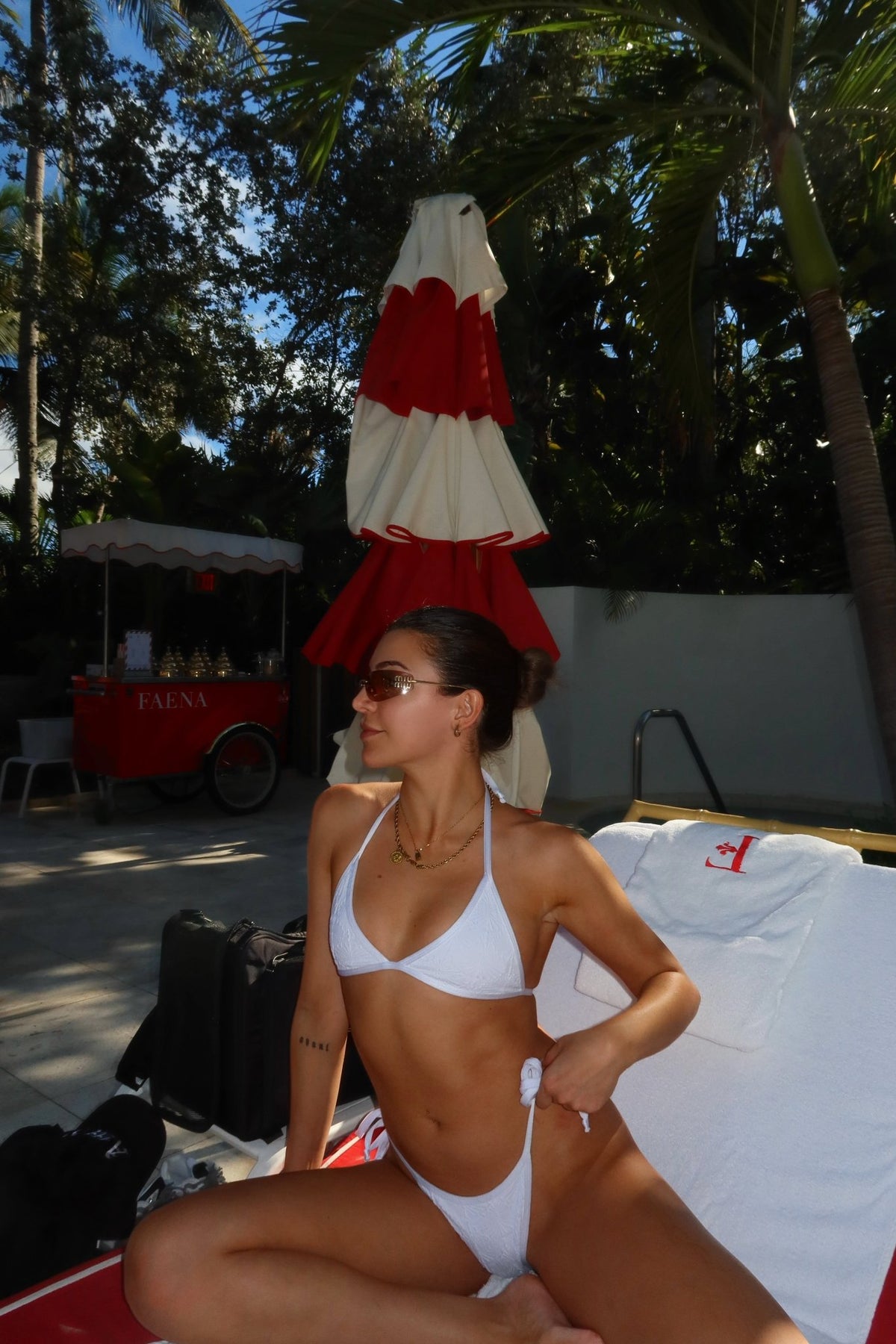 Woman in a white reversible bikini lounging by the pool with palm trees and a red umbrella