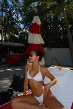 Woman in a white reversible bikini lounging by the pool with palm trees and a red umbrella