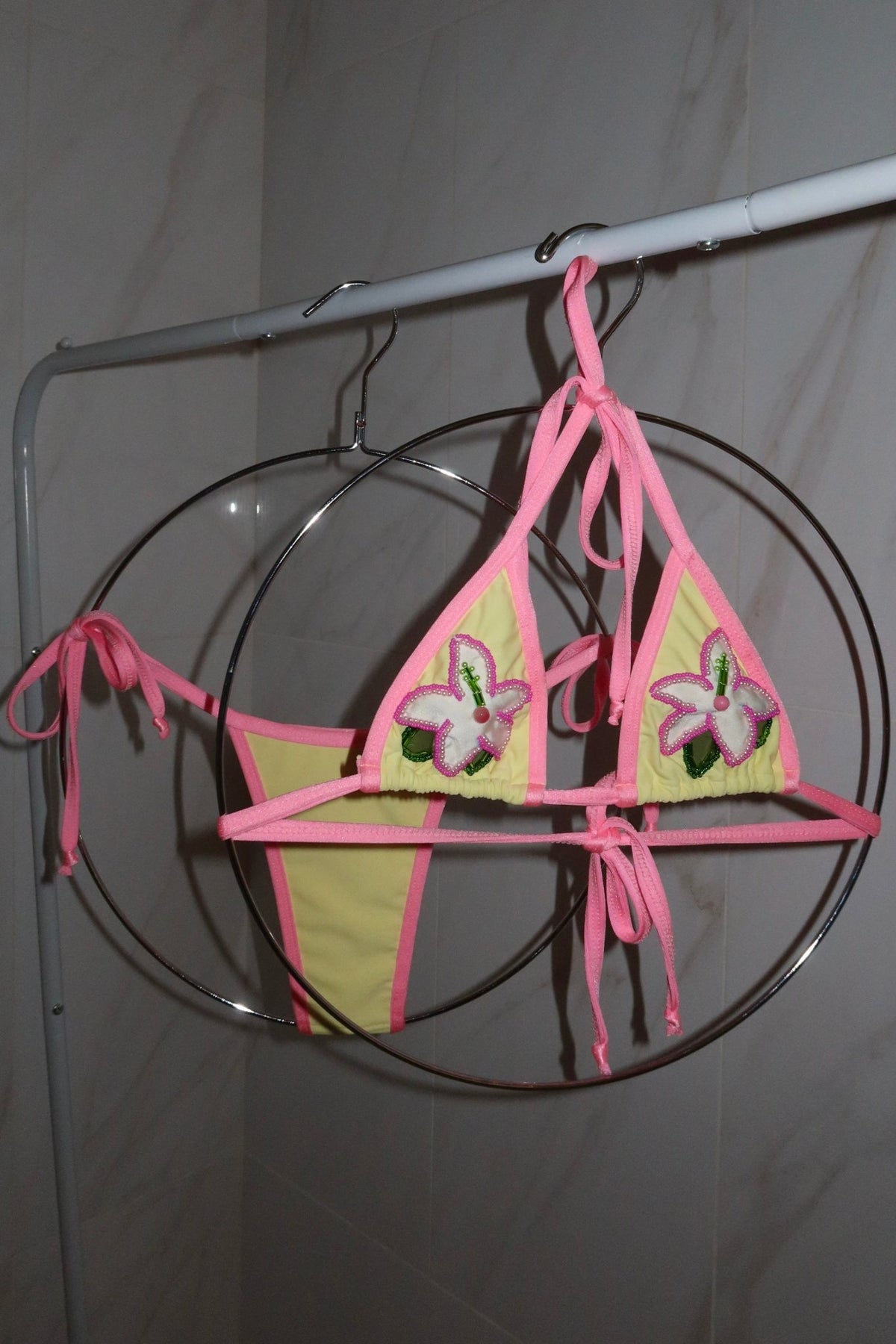Handmade yellow and pink bikini set with floral bead details hanging on round rack