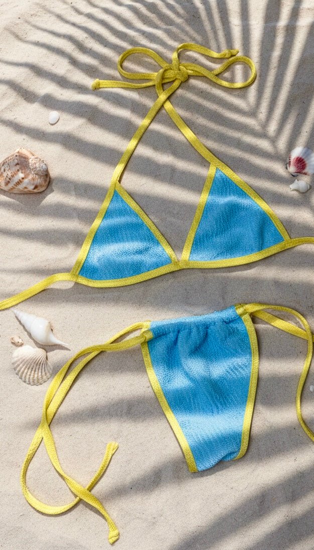 Blue and yellow reversible bikini set on sand with seashells, summer swimwear flat lay
