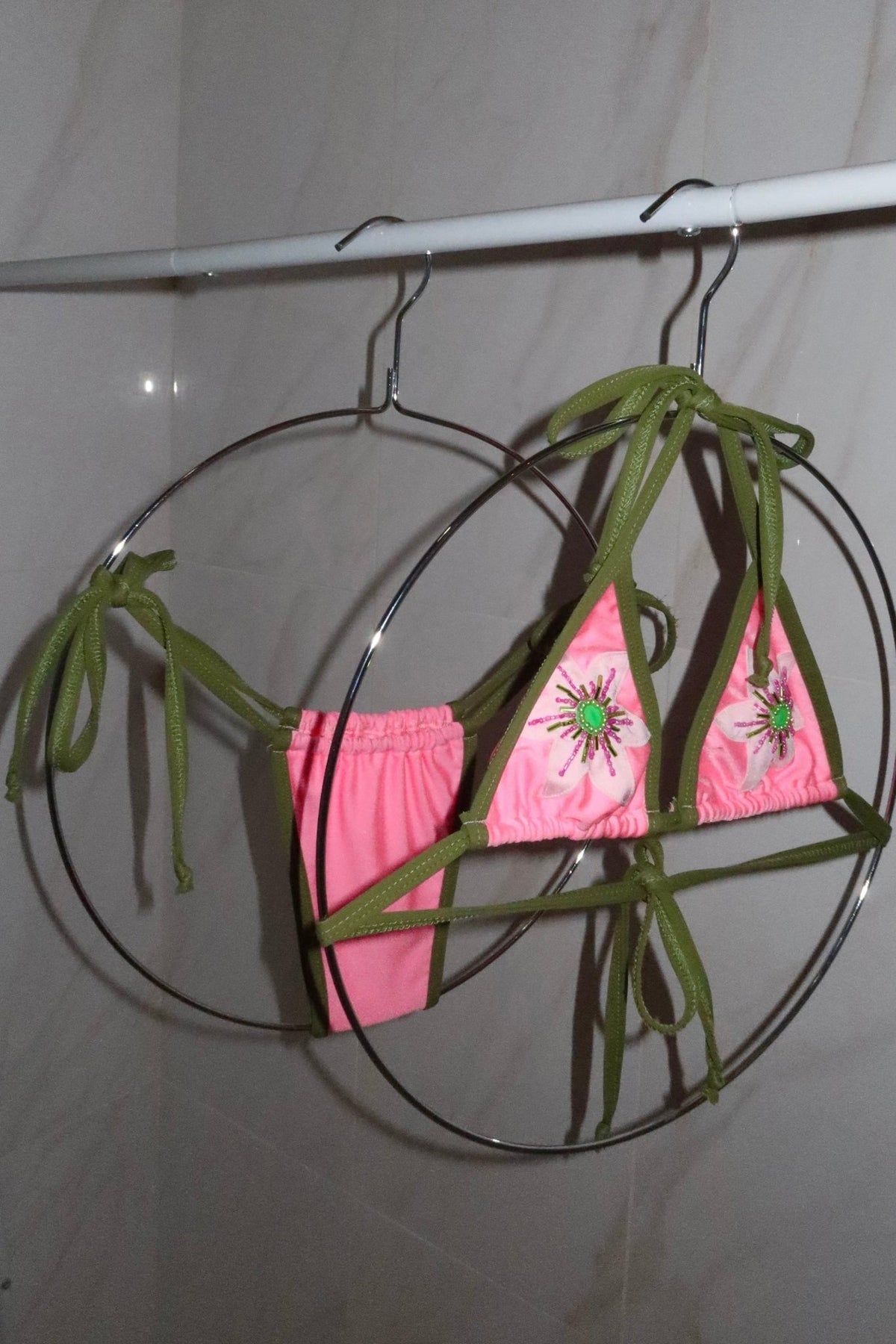 Handmade pink and green bikini with beaded floral details hanging on circular hangers