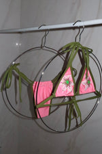 Handmade pink and green bikini with beaded floral details hanging on circular hangers
