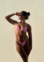 Woman modeling a handmade pink triangle bikini with thin straps in natural sunlight