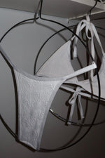 White textured bikini set with tie straps on metal hangers, reversible swimwear