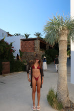 Woman in a handmade red bikini and sun hat posing outdoors by palm trees and resort buildings