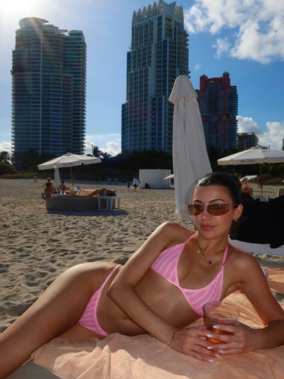 Woman in a pink bikini lounging on a beach chair, with modern city buildings in the background