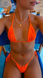 Woman wearing a handmade orange string bikini sitting on a blue beach chair