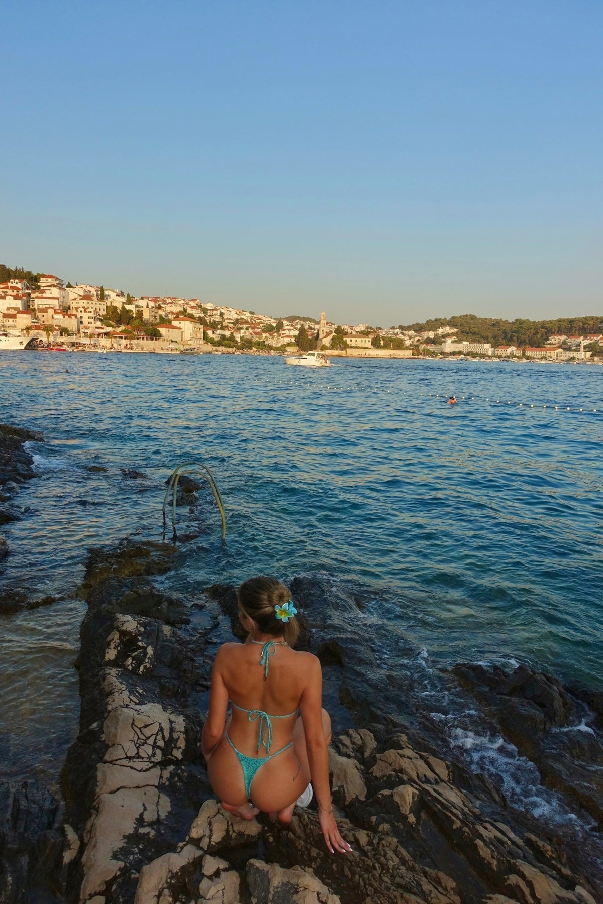Woman in handmade turquoise bikini sitting on rocky shore by the sea with ocean view
