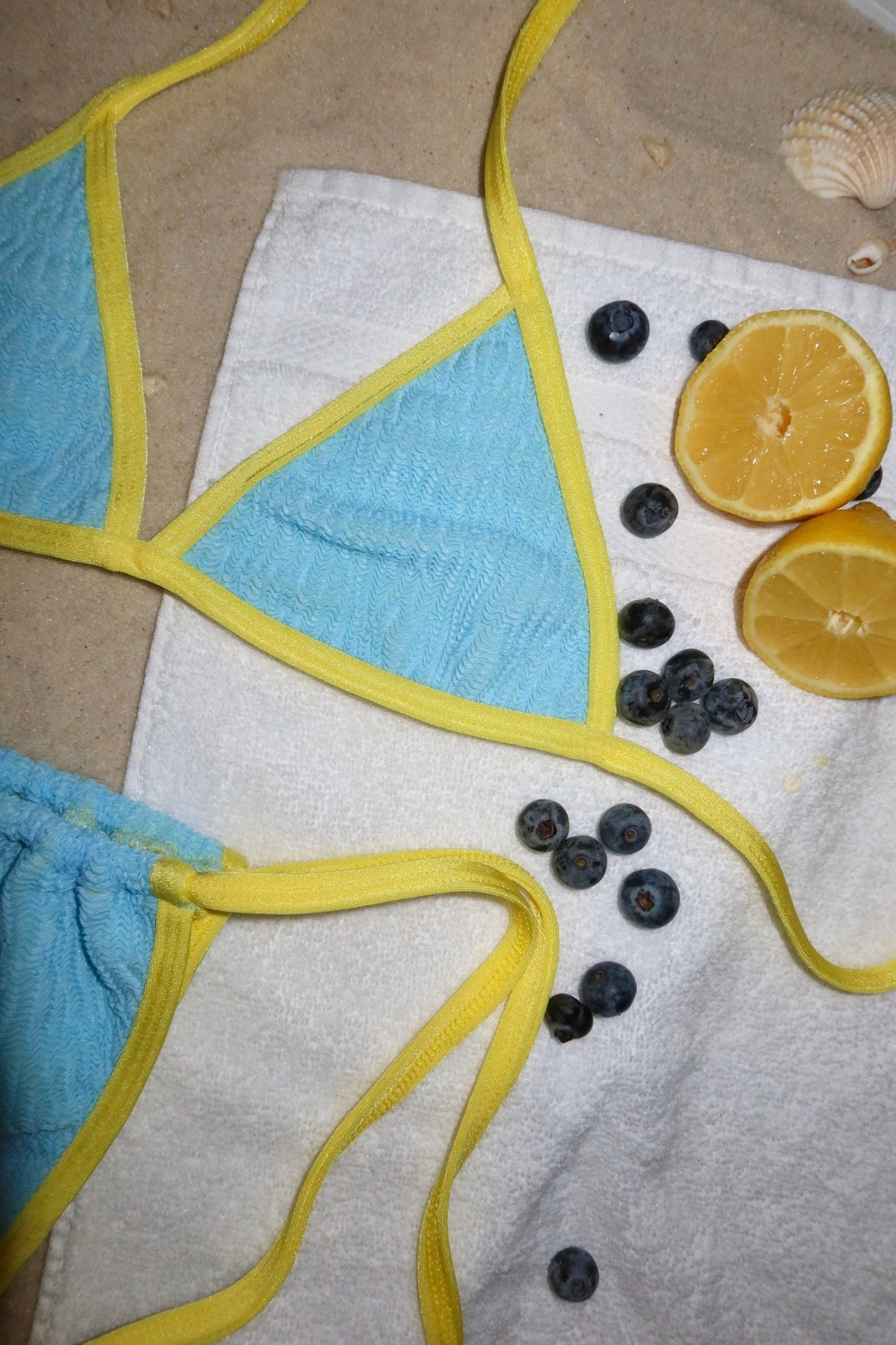 Blue and yellow bikini on a white towel with blueberries and lemons on sand
