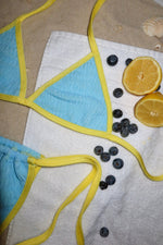 Blue and yellow bikini on a white towel with blueberries and lemons on sand