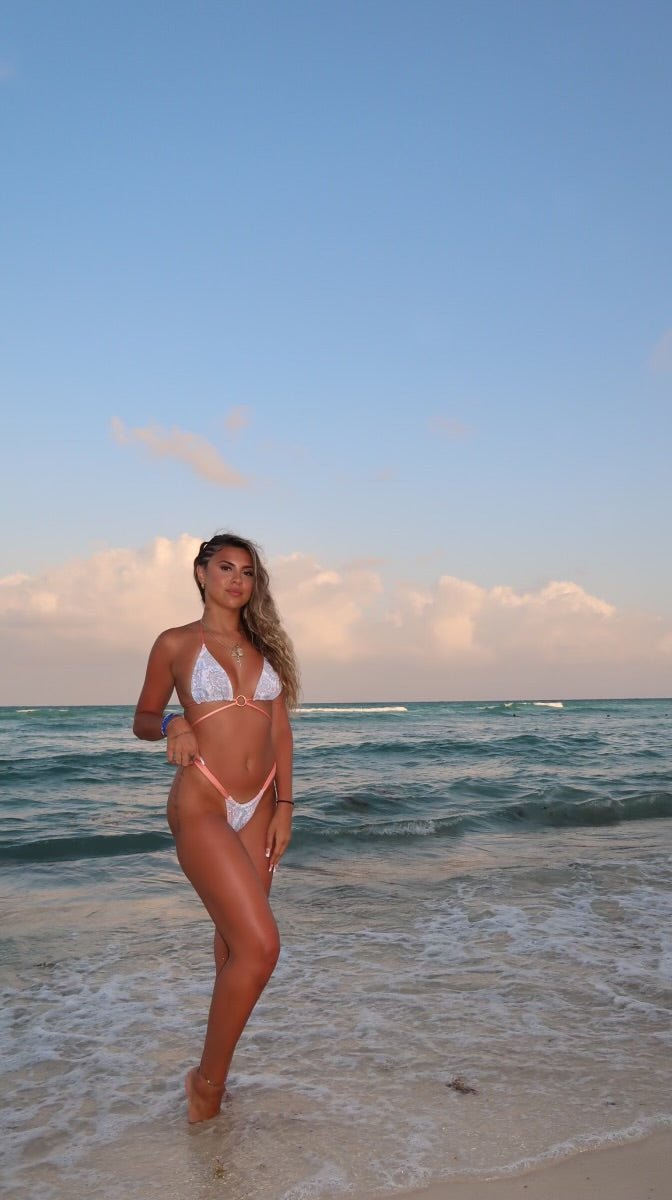 Woman wearing handmade white bikini with pink trim on a sandy beach at sunset