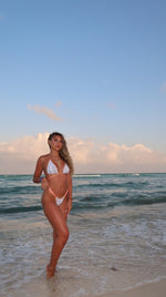 Woman wearing handmade white bikini with pink trim on a sandy beach at sunset