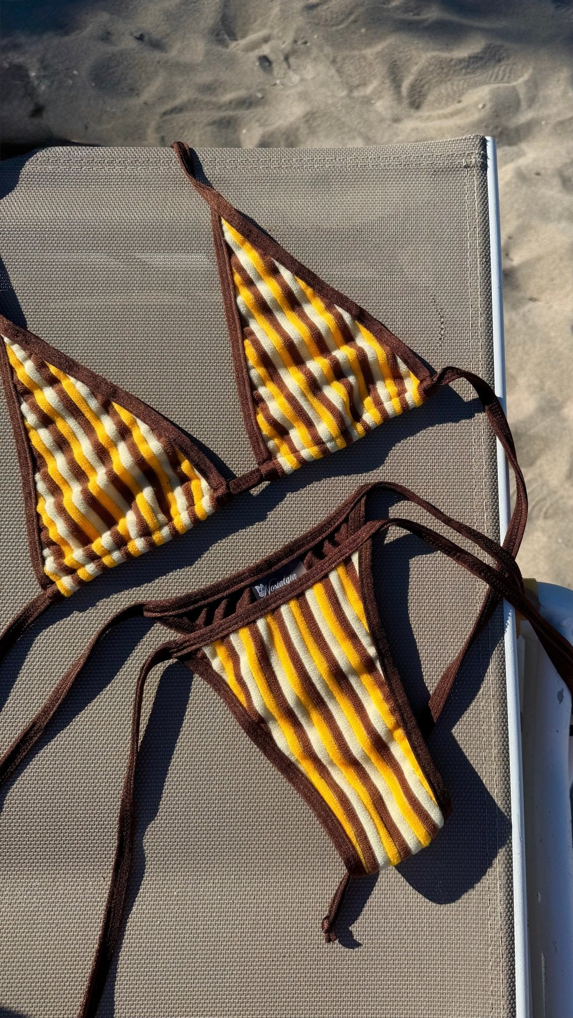 Yellow and brown striped handmade bikini set on a lounge chair at the beach