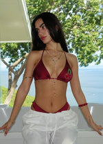 Woman wearing a burgundy cherry bikini top and white pants near window with ocean view