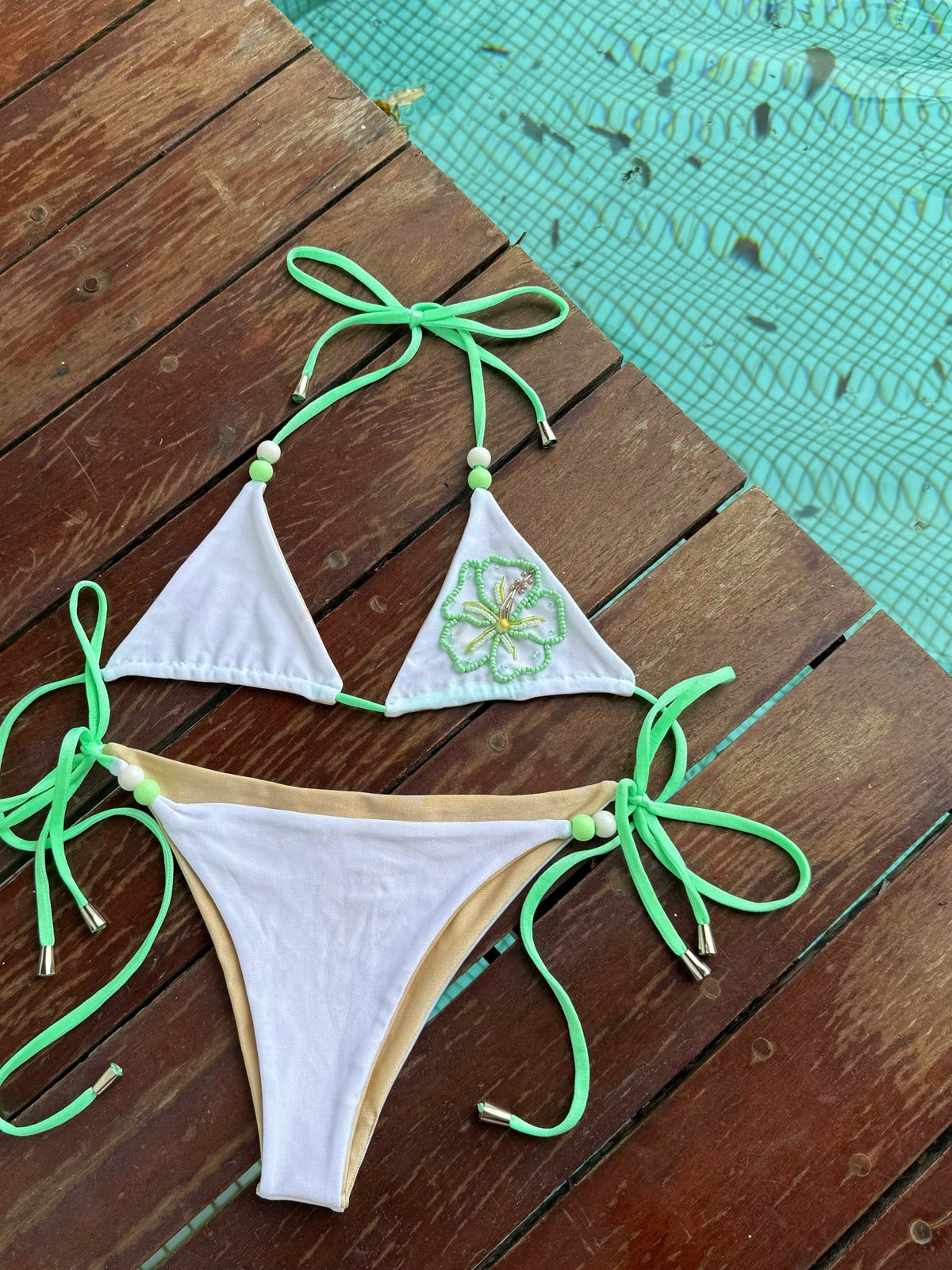 White and green reversible bikini with beaded trim on wooden deck by pool