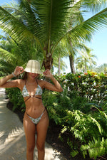 Woman in patterned string bikini and sun hat posing by tropical palm trees
