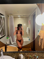 Woman in a brown triangle bikini taking a mirror selfie in a modern bathroom.