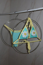 Turquoise and yellow handmade triangle bikini with daisy embroidery, displayed on hangers