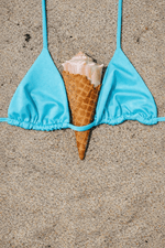 Blue bikini top with a seashell and waffle cone on sand, beach swimwear concept