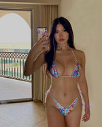 Woman in floral string bikini taking mirror selfie indoors with balcony and sea view