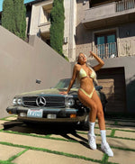 Woman in a yellow bikini posing by a vintage Mercedes car in a sunny backyard