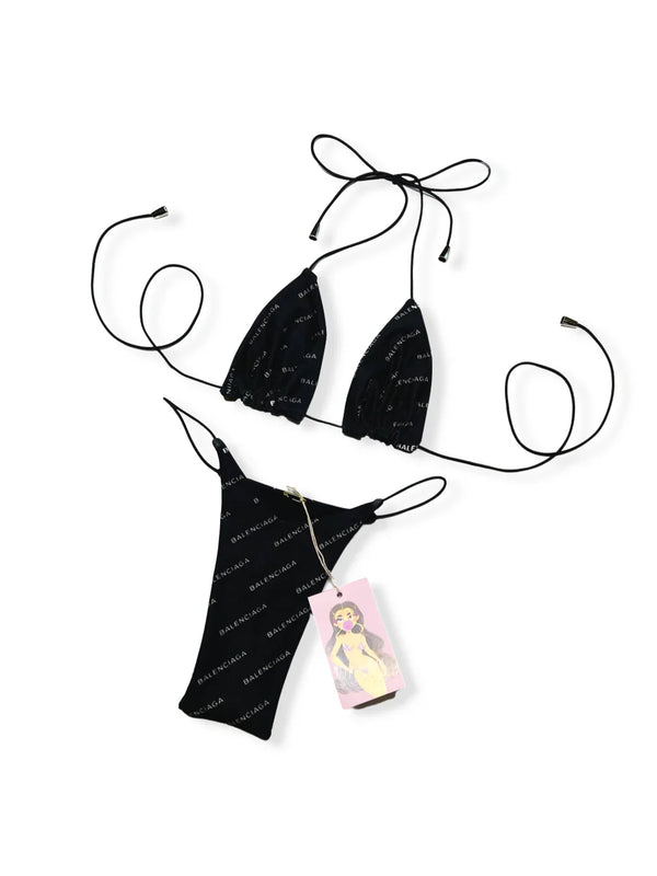 Black string bikini set with white text print and a pink illustrated tag, laid flat on white background